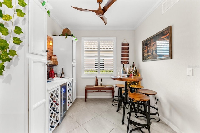 tiled dining space with bar area, crown molding, and ceiling fan