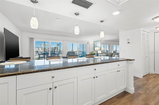 kitchen featuring visible vents, open floor plan, pendant lighting, wood finished floors, and white cabinetry