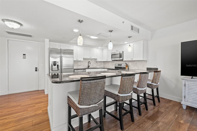 kitchen with wood finished floors, visible vents, a sink, decorative backsplash, and stainless steel appliances