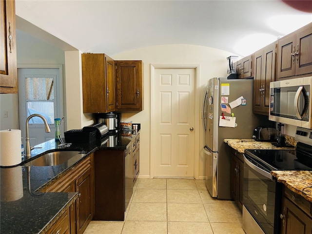 kitchen with vaulted ceiling, dark stone countertops, sink, light tile patterned flooring, and appliances with stainless steel finishes