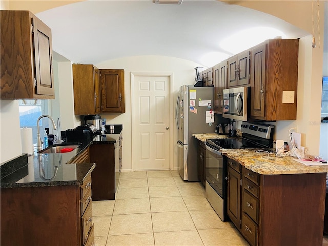 kitchen with vaulted ceiling, dark stone countertops, sink, light tile patterned flooring, and appliances with stainless steel finishes