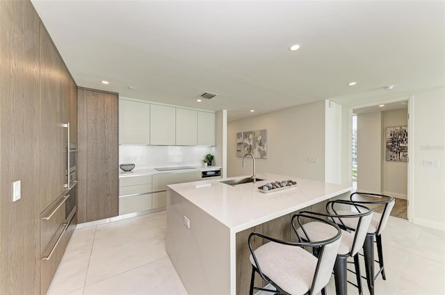 kitchen featuring a breakfast bar, a sink, visible vents, an island with sink, and modern cabinets