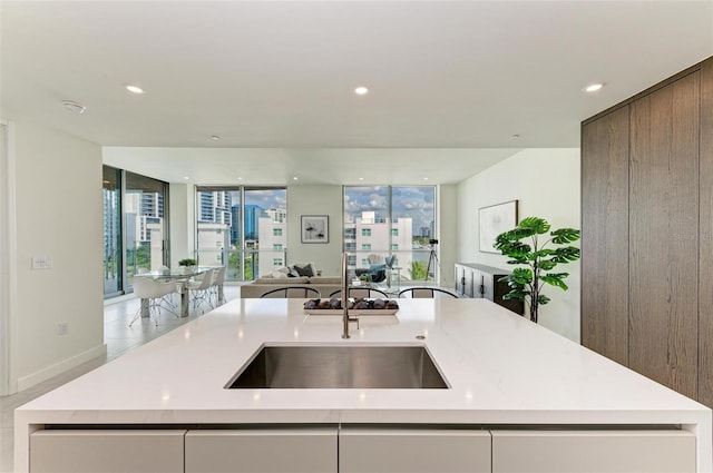 kitchen with recessed lighting, light countertops, open floor plan, a sink, and an island with sink