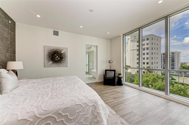 bedroom featuring recessed lighting, a city view, wood finished floors, visible vents, and ensuite bath