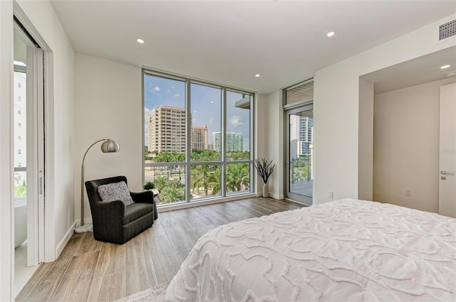 bedroom with recessed lighting, a city view, wood finished floors, access to outside, and a wall of windows