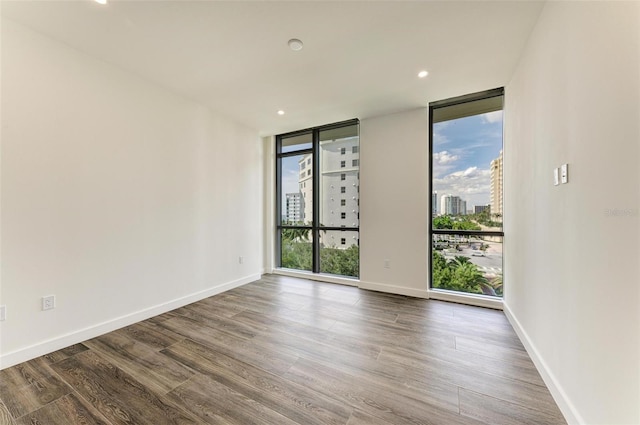 unfurnished room with baseboards, a view of city, wood finished floors, and floor to ceiling windows