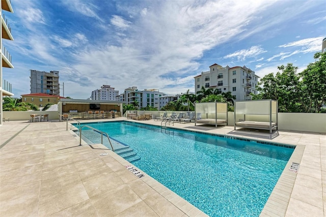 pool featuring a city view, a patio, outdoor dry bar, and fence