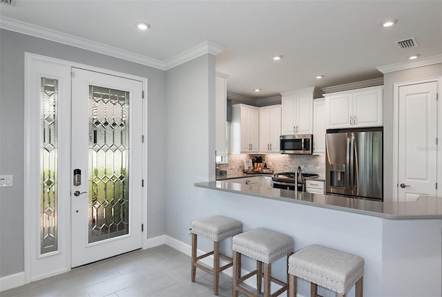 kitchen featuring kitchen peninsula, stainless steel appliances, crown molding, white cabinets, and light tile patterned flooring