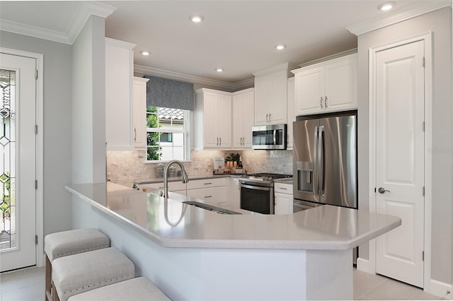 kitchen with kitchen peninsula, ornamental molding, appliances with stainless steel finishes, white cabinetry, and a breakfast bar area