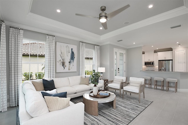 living room with ceiling fan, light tile patterned flooring, a raised ceiling, and crown molding