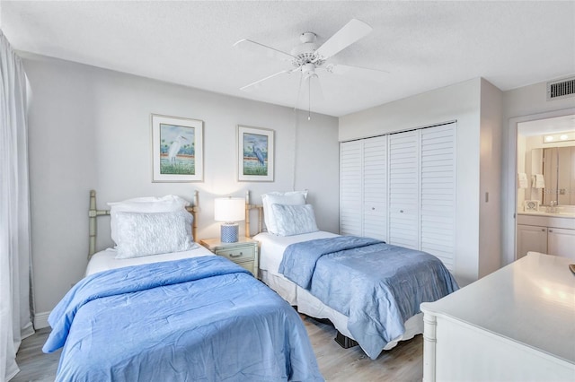 bedroom featuring ensuite bathroom, a textured ceiling, ceiling fan, light hardwood / wood-style floors, and a closet