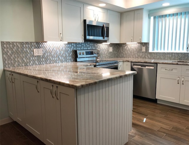 kitchen with tasteful backsplash, white cabinetry, stainless steel appliances, and dark wood-type flooring