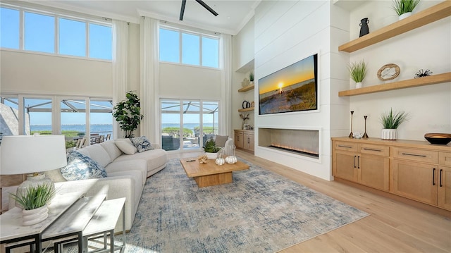 living room with plenty of natural light, light wood-type flooring, a towering ceiling, and crown molding