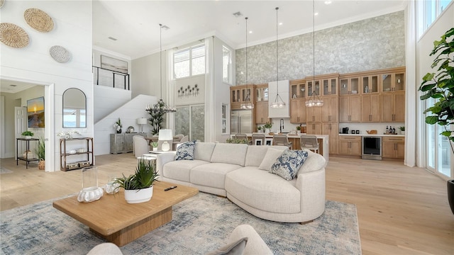 living room with crown molding, light hardwood / wood-style flooring, beverage cooler, and a high ceiling