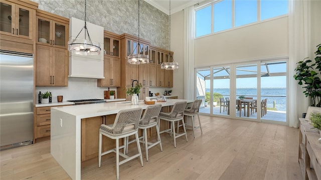 kitchen featuring a water view, hanging light fixtures, a towering ceiling, ornamental molding, and stainless steel appliances