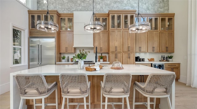 kitchen featuring a notable chandelier, stainless steel built in fridge, decorative light fixtures, light wood-type flooring, and a large island