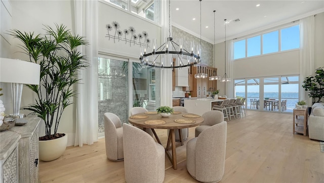 dining area with a notable chandelier, a towering ceiling, light hardwood / wood-style floors, a water view, and ornamental molding