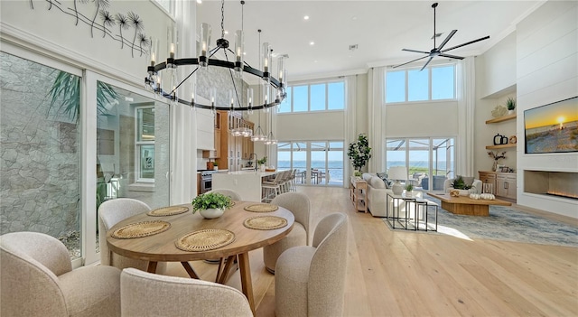 dining space with a high ceiling, an inviting chandelier, sink, ornamental molding, and light hardwood / wood-style floors