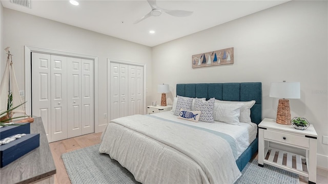 bedroom with ceiling fan, wood-type flooring, and two closets