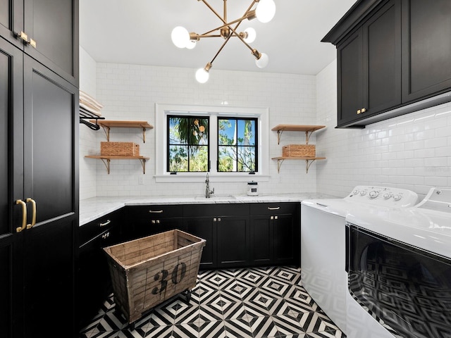 clothes washing area with a chandelier, washer and clothes dryer, cabinets, and sink