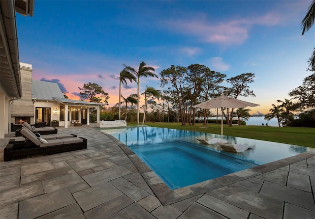 pool at dusk featuring a patio area, a yard, and an in ground hot tub