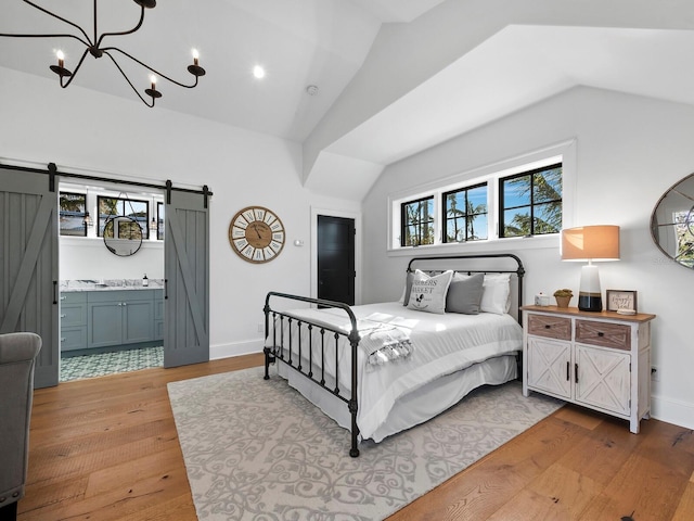 bedroom featuring lofted ceiling, an inviting chandelier, ensuite bath, a barn door, and light hardwood / wood-style floors