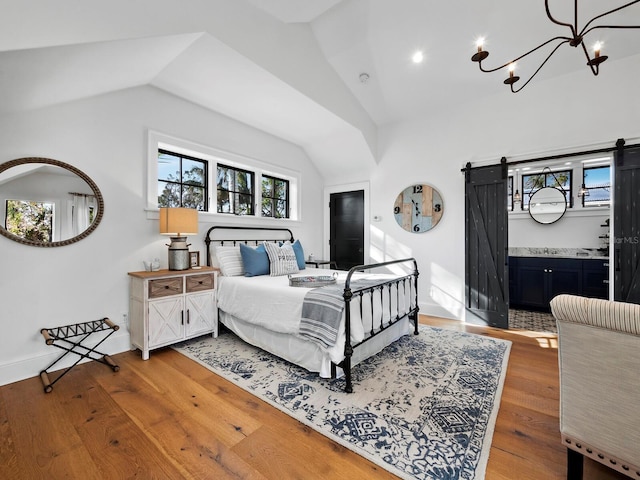 bedroom featuring a barn door, a chandelier, wood-type flooring, and lofted ceiling