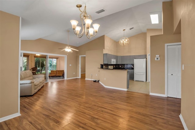 unfurnished living room featuring ceiling fan with notable chandelier, light hardwood / wood-style floors, and vaulted ceiling