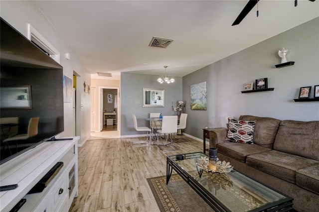living room with light wood-type flooring and ceiling fan with notable chandelier