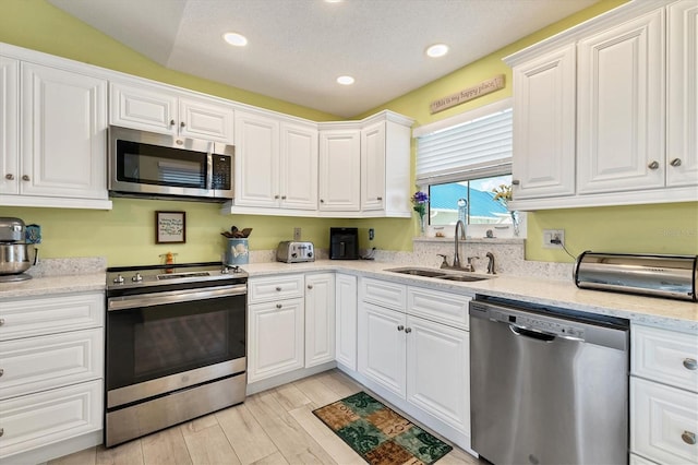 kitchen with light stone countertops, lofted ceiling, white cabinetry, stainless steel appliances, and sink