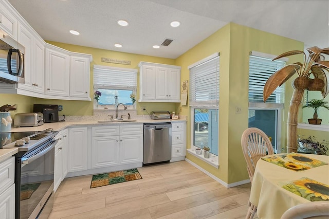 kitchen with light stone countertops, appliances with stainless steel finishes, white cabinetry, sink, and light hardwood / wood-style flooring