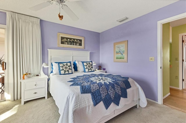 bedroom featuring ceiling fan, light colored carpet, and a textured ceiling