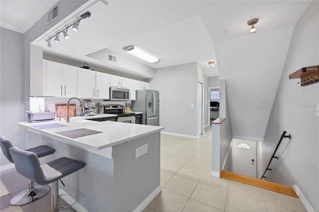 kitchen with stainless steel appliances, light tile patterned flooring, white cabinetry, kitchen peninsula, and a kitchen bar