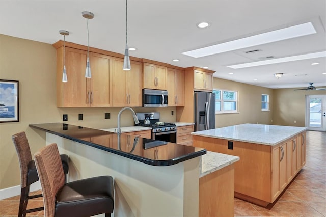 kitchen with kitchen peninsula, appliances with stainless steel finishes, a kitchen breakfast bar, dark stone counters, and pendant lighting