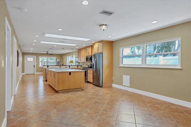 kitchen featuring appliances with stainless steel finishes, light tile patterned floors, a kitchen island, and a wealth of natural light