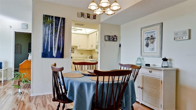 dining room with ceiling fan with notable chandelier, light hardwood / wood-style flooring, and a textured ceiling