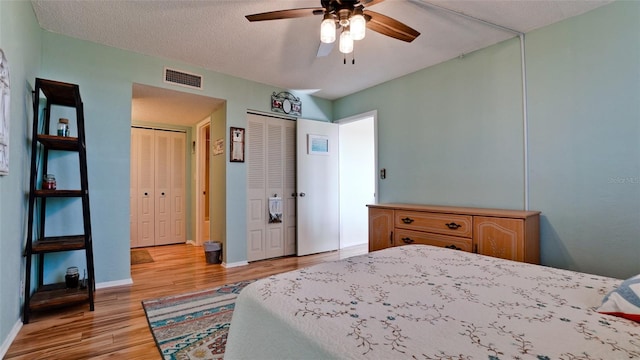 bedroom featuring a textured ceiling, light wood-type flooring, ceiling fan, and two closets