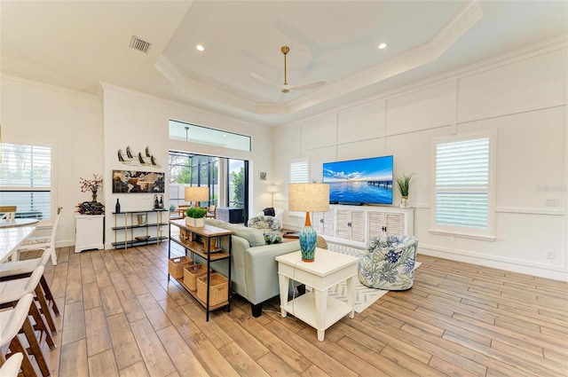 living room with light wood-type flooring, a tray ceiling, ceiling fan, and ornamental molding