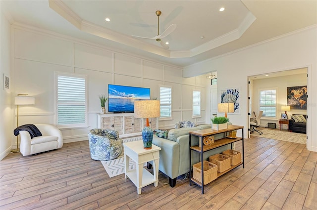 living room with a raised ceiling, crown molding, light hardwood / wood-style flooring, and ceiling fan