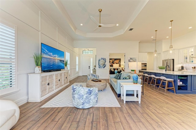 living room with a raised ceiling, ceiling fan, crown molding, and light hardwood / wood-style floors