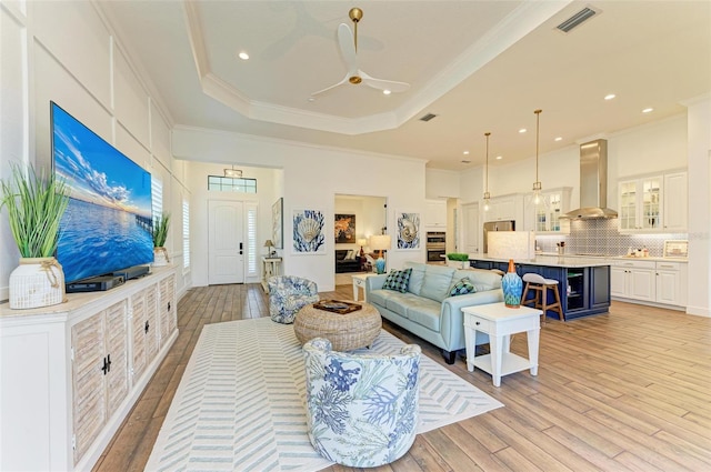 living room featuring ceiling fan, crown molding, light wood-type flooring, and a raised ceiling