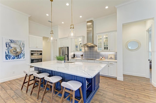 kitchen featuring a large island with sink, white cabinets, and wall chimney range hood