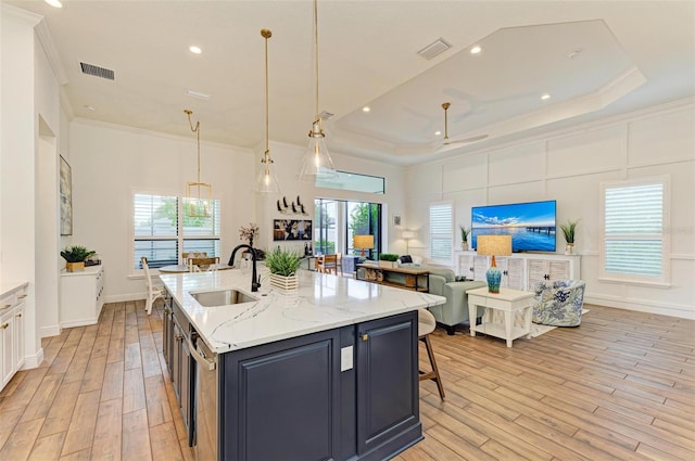 kitchen with hanging light fixtures, light hardwood / wood-style floors, a kitchen island with sink, and sink