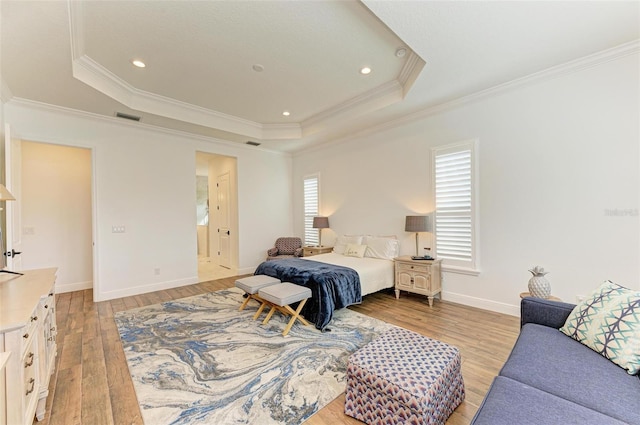 bedroom featuring light wood-type flooring, a tray ceiling, ornamental molding, and connected bathroom