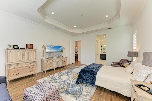 bedroom with crown molding, ensuite bathroom, light hardwood / wood-style floors, and a raised ceiling