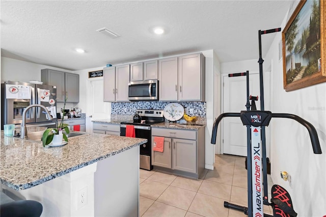 kitchen with gray cabinetry, sink, a textured ceiling, light stone counters, and stainless steel appliances