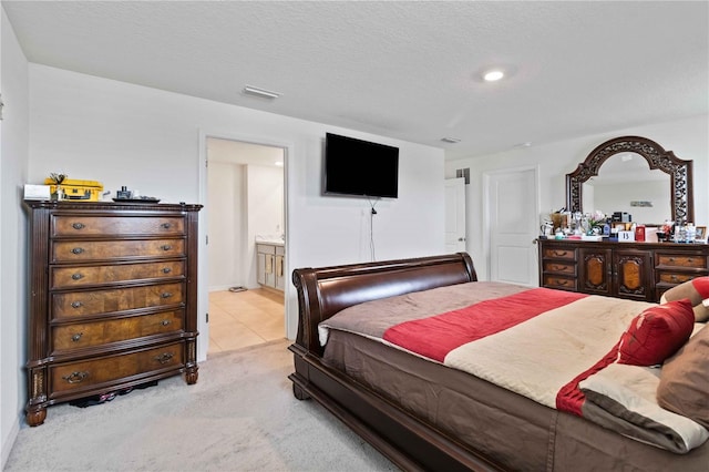 bedroom with light carpet, a textured ceiling, and ensuite bath