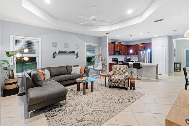 tiled living room featuring ceiling fan and a tray ceiling