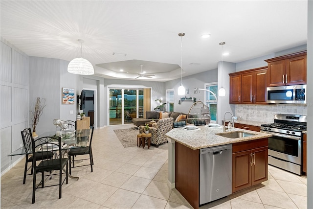 kitchen featuring stainless steel appliances, a raised ceiling, a center island with sink, ceiling fan, and sink