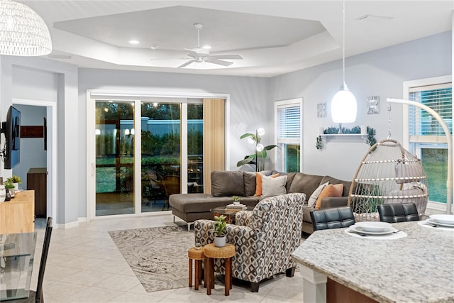 tiled living room with a raised ceiling, ceiling fan, and a wealth of natural light